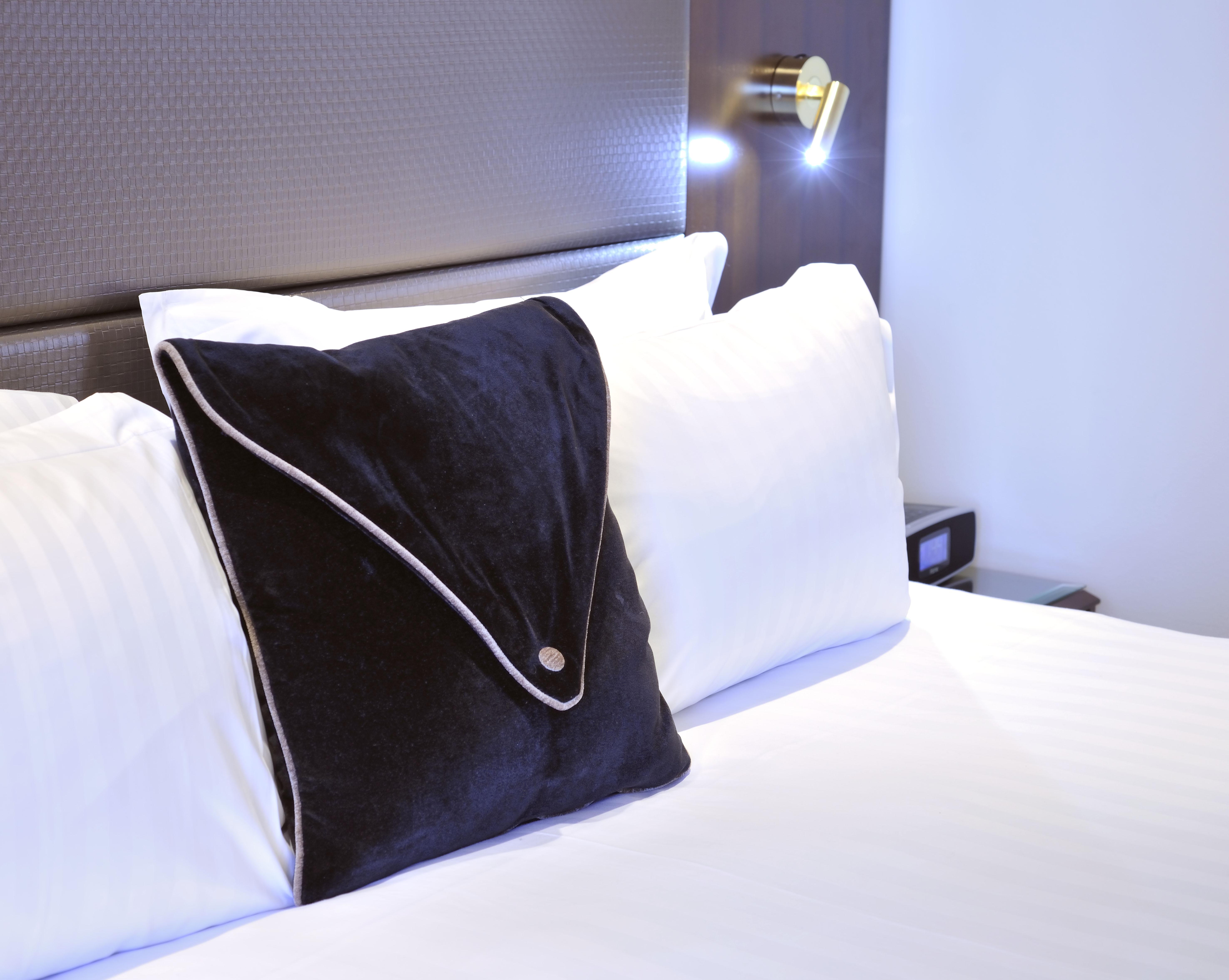 Stamford Plaza Melbourne Hotel Exterior foto The photo shows a neatly arranged bed with white linens. There are several pillows, with one black pillow featuring a distinctive design on top of the white pillows. The headboard of the bed is visible, along with a stylish wall-mounted light fixture