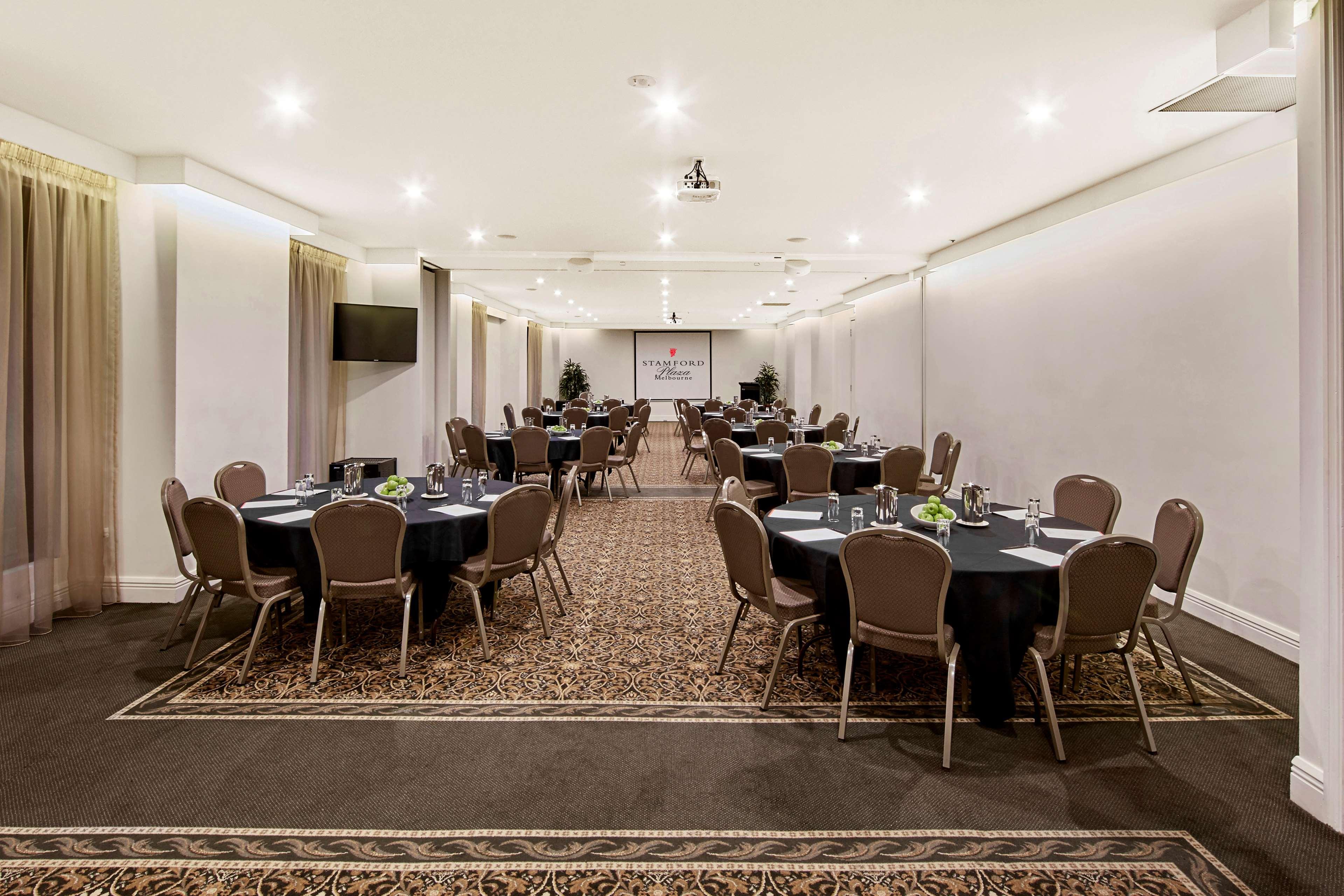 Stamford Plaza Melbourne Hotel Exterior foto The photo shows an event space or banquet hall set up for a gathering. The room features several round tables covered with black tablecloths, each adorned with small centerpieces. Chairs are arranged around each table. The lighting is bright and mode