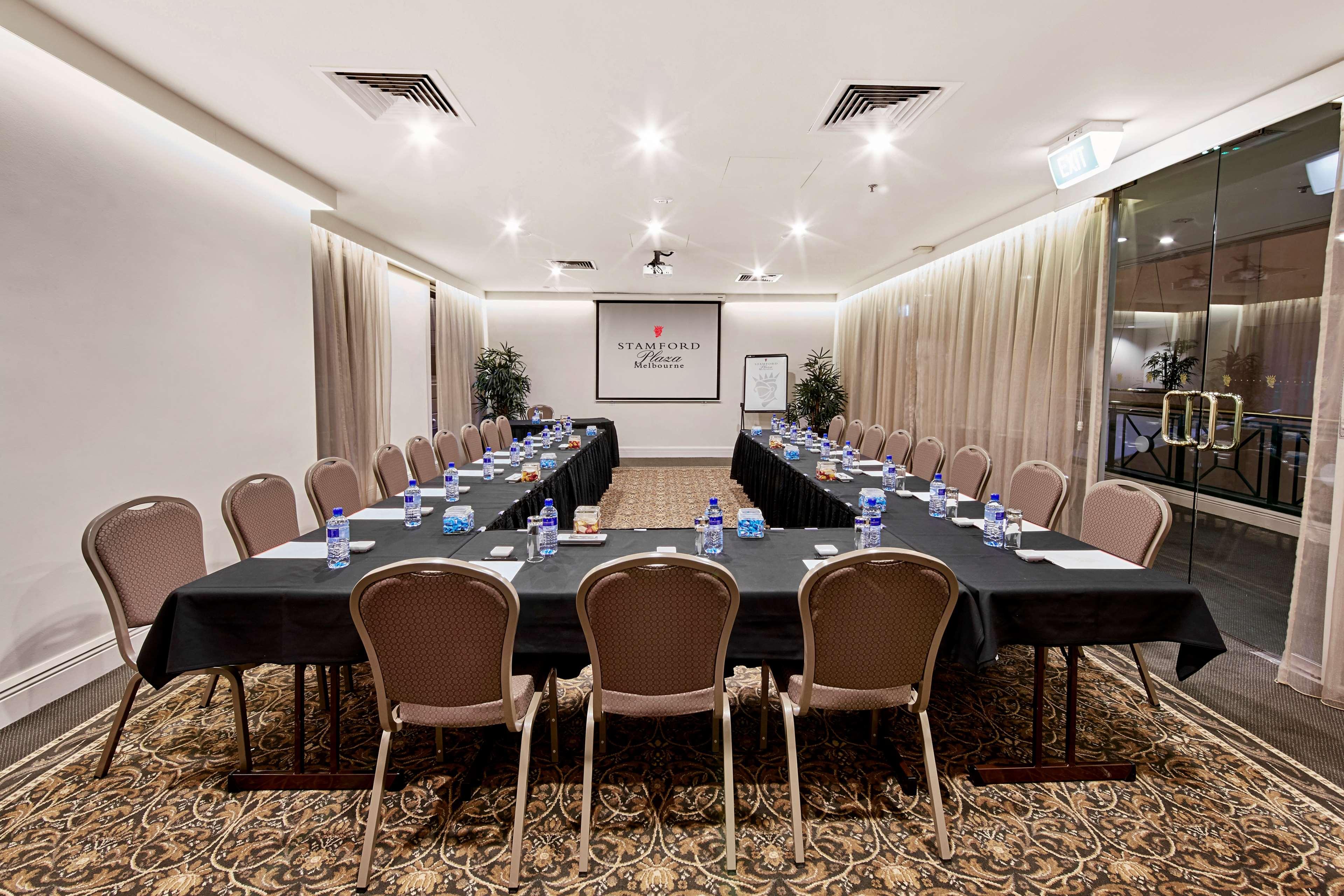 Stamford Plaza Melbourne Hotel Exterior foto The photo shows a conference room set up for a meeting. There are several long tables arranged in a U-shape, covered with black tablecloths. Each table has a water bottle and notepad placed at intervals. The room is well-lit, with light-colored walls