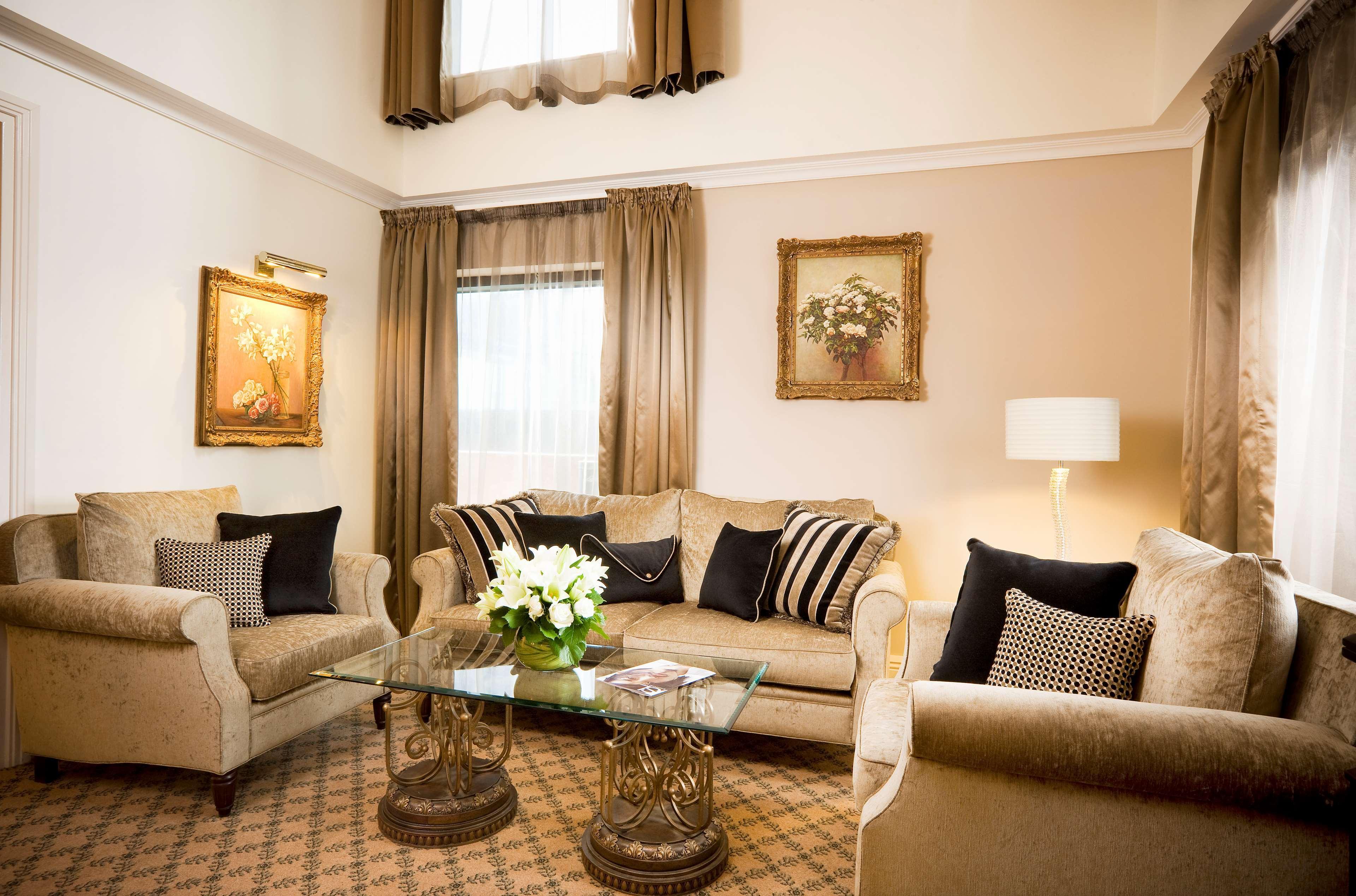 Stamford Plaza Melbourne Hotel Quarto foto The photo depicts a stylish living room with a warm and inviting aesthetic. It features a set of comfortable beige sofas adorned with decorative pillows in black and patterned designs. There is a glass coffee table at the center, supported by elegant