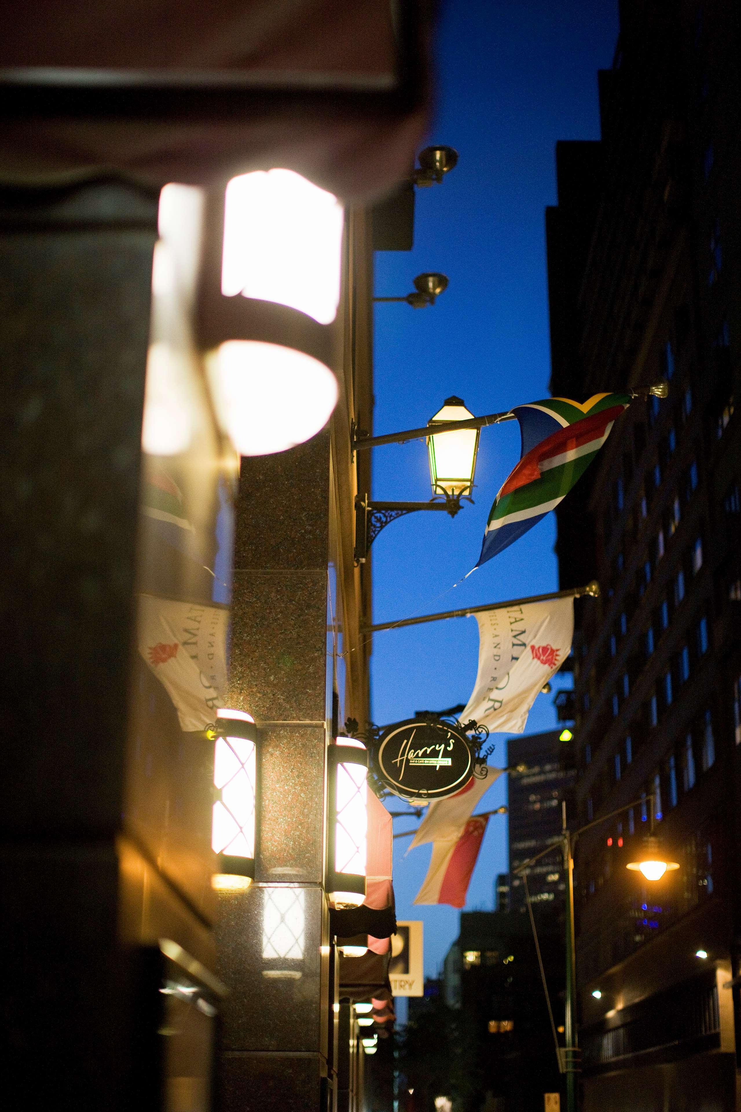 Stamford Plaza Melbourne Hotel Exterior foto The photo features a street view of a building at dusk. Prominently displayed are several flags, including a South African flag, which are fluttering in the wind. There is a sign that reads "Harry's," likely indicating the name of a business or estab