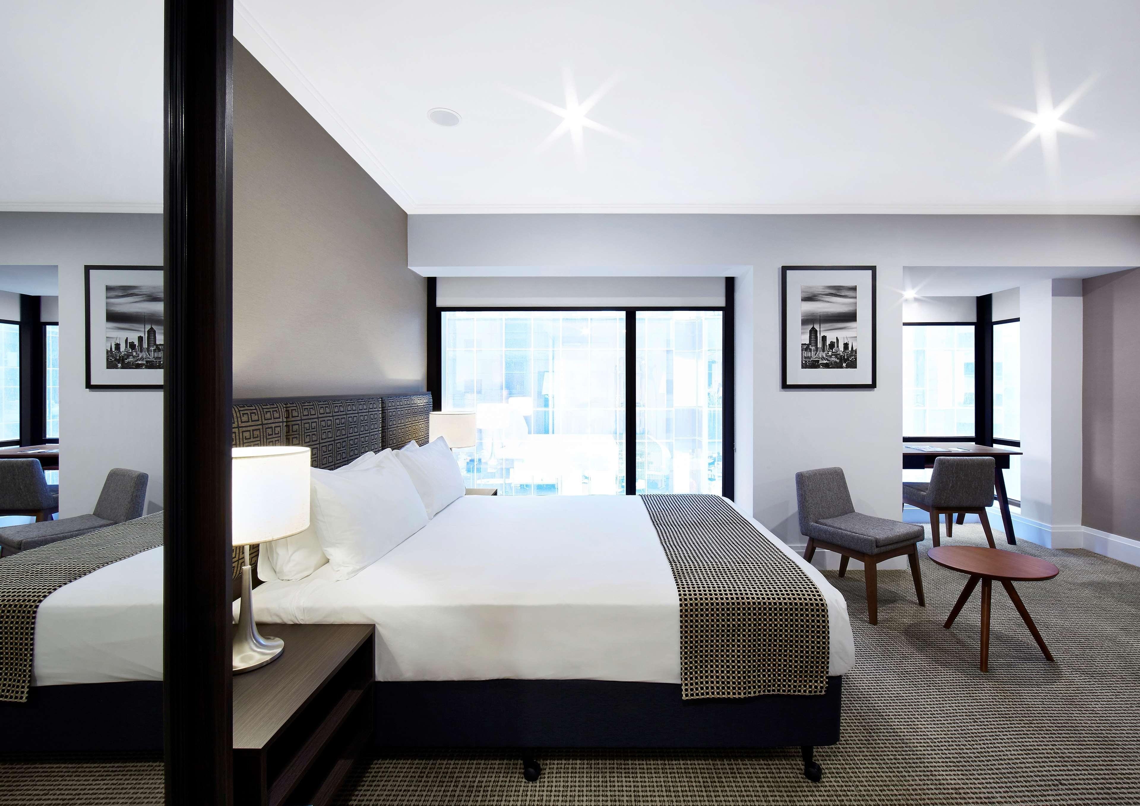 Stamford Plaza Melbourne Hotel Exterior foto The image shows a modern hotel room featuring a large bed with white linens and a gray throw blanket. There are two windows that allow natural light to enter the space, and the walls are painted in a light color. In addition to the bed, there are two