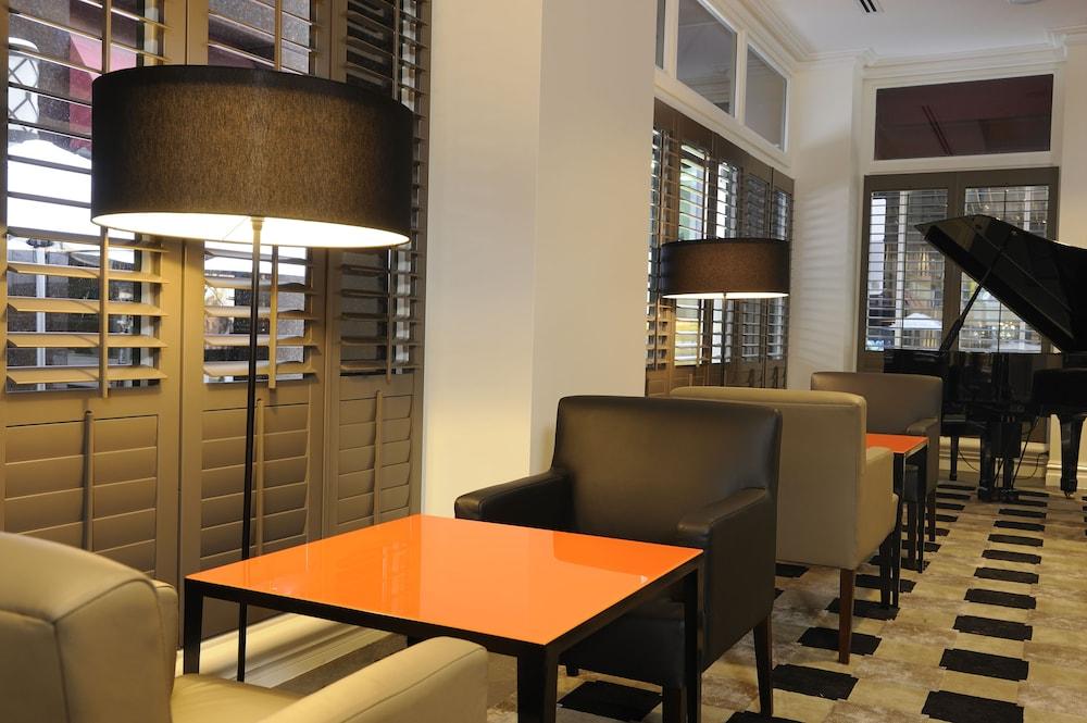 Stamford Plaza Melbourne Hotel Exterior foto The photo shows a cozy interior space, likely a lounge or café. It features a modern design with a mix of seating options, including black and light-colored chairs surrounding small tables. One table has a bright orange top, creating a striking visua