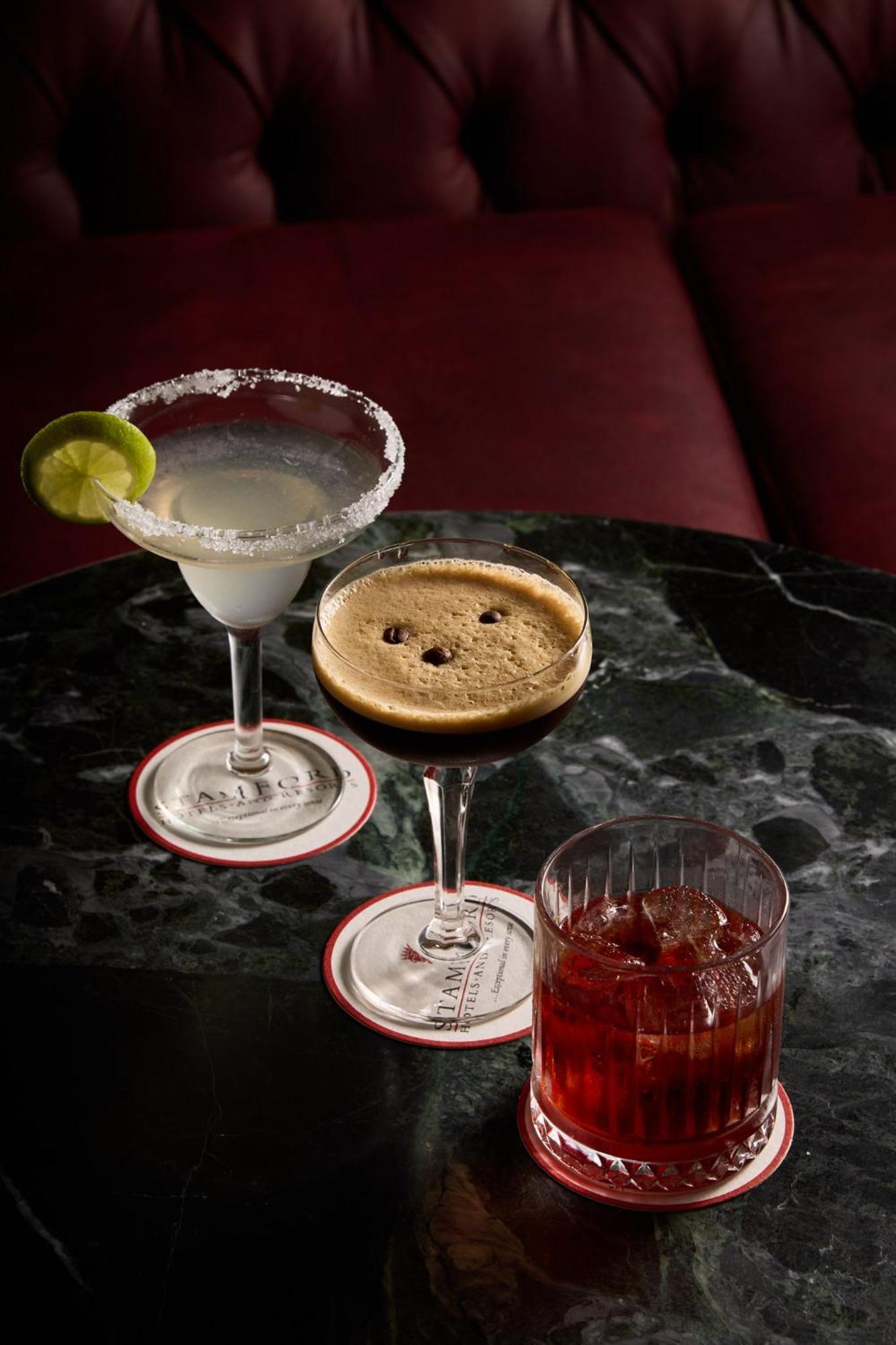 Stamford Plaza Melbourne Hotel Exterior foto The photo displays three different cocktails arranged on a dark marble table. 

1. On the left, there is a margarita glass filled with a clear drink, garnished with a lime slice and featuring a salted rim.
2. In the center, a coupe glass holds a dark