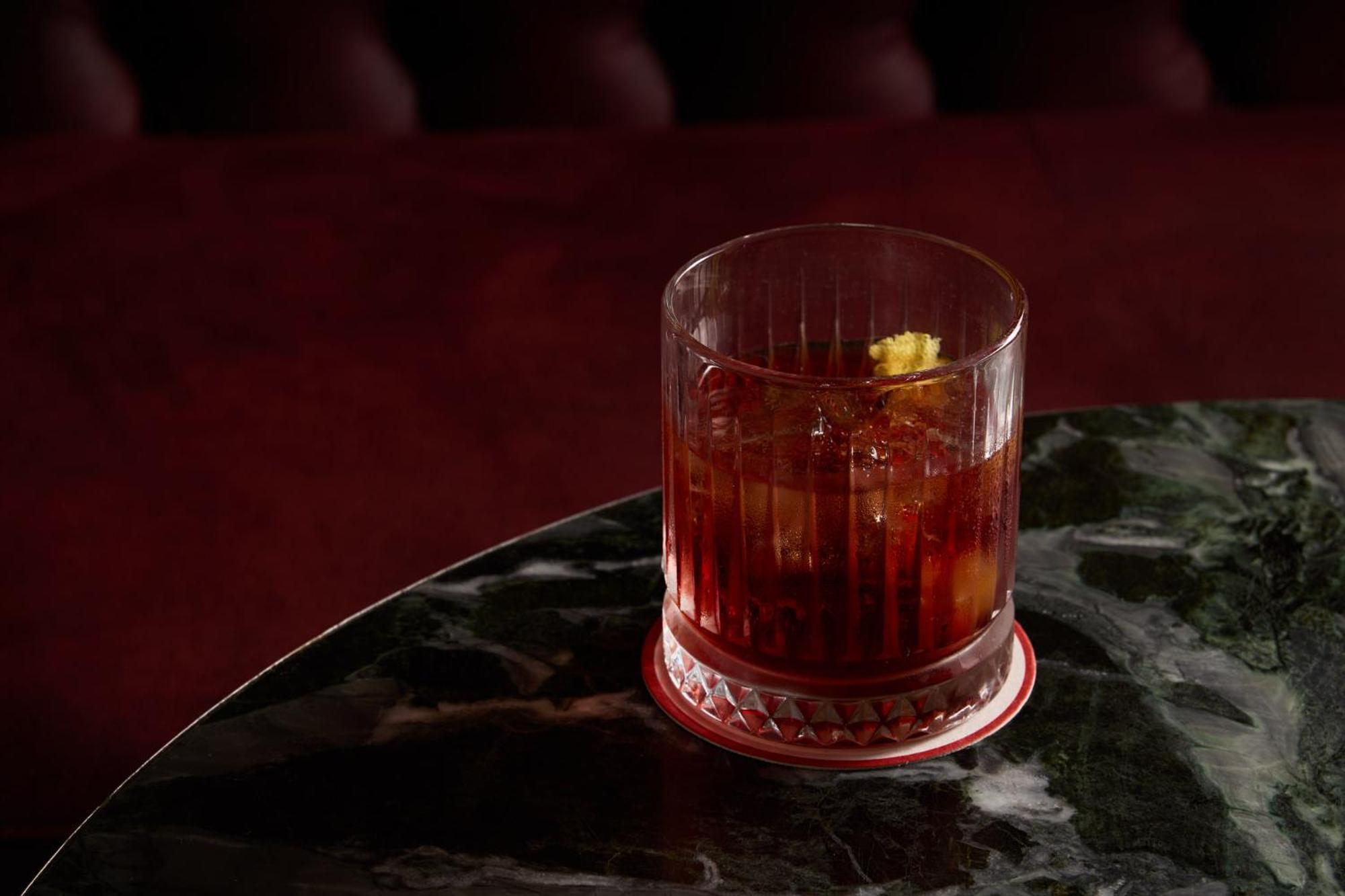 Stamford Plaza Melbourne Hotel Exterior foto The photo depicts a short glass filled with a dark-colored beverage, likely an alcoholic drink. The glass has a textured design, with ice cubes visible inside. A twist of lemon peel is perched on the rim, adding a touch of garnish. The drink sits on 