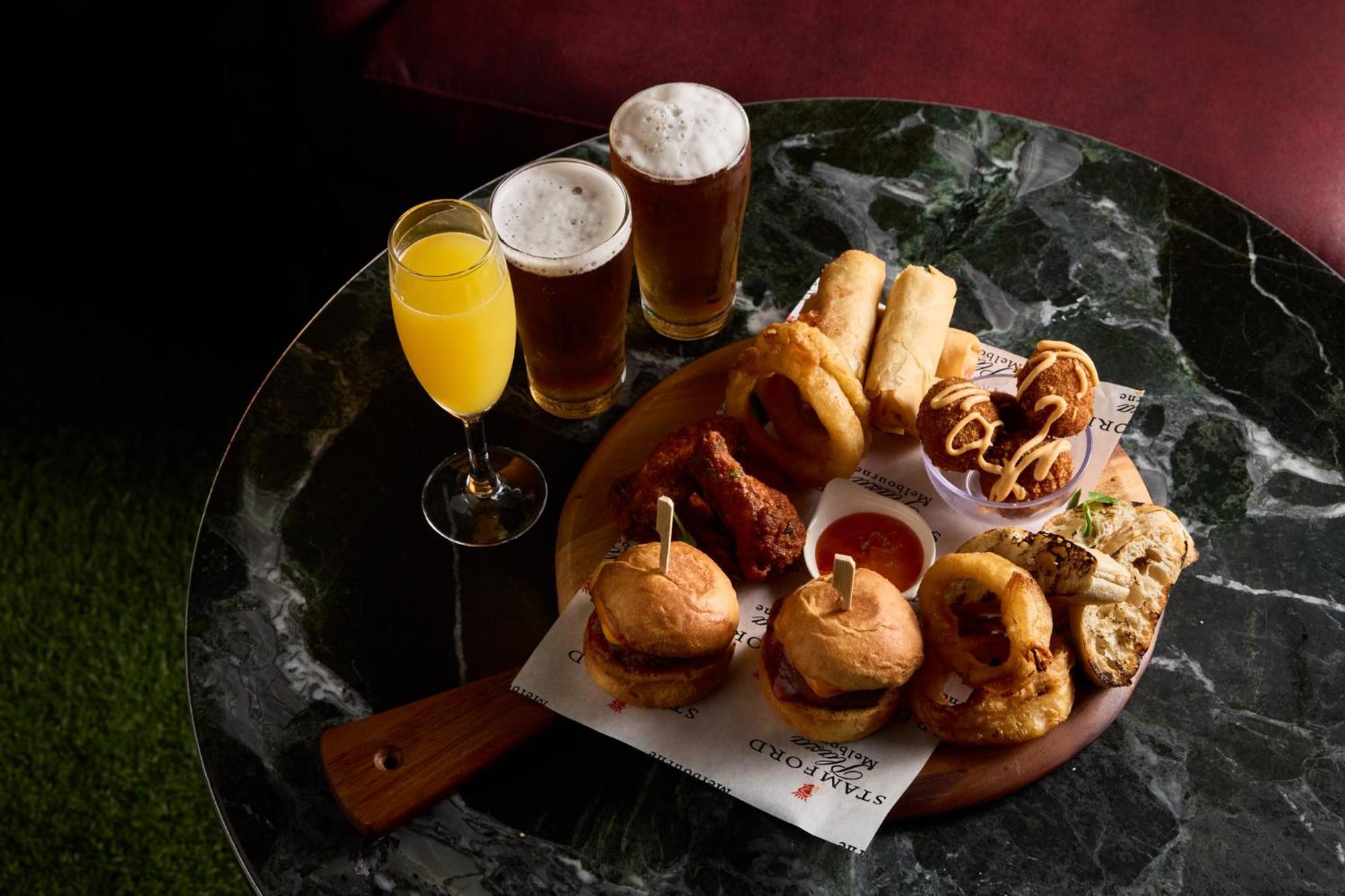 Stamford Plaza Melbourne Hotel Exterior foto The photo displays a variety of food and drinks arranged on a marble table. There are small burgers garnished with skewers, crispy chicken pieces, and deep-fried snacks. Additionally, there are two glasses of beer and a cocktail, likely a mimosa, pre