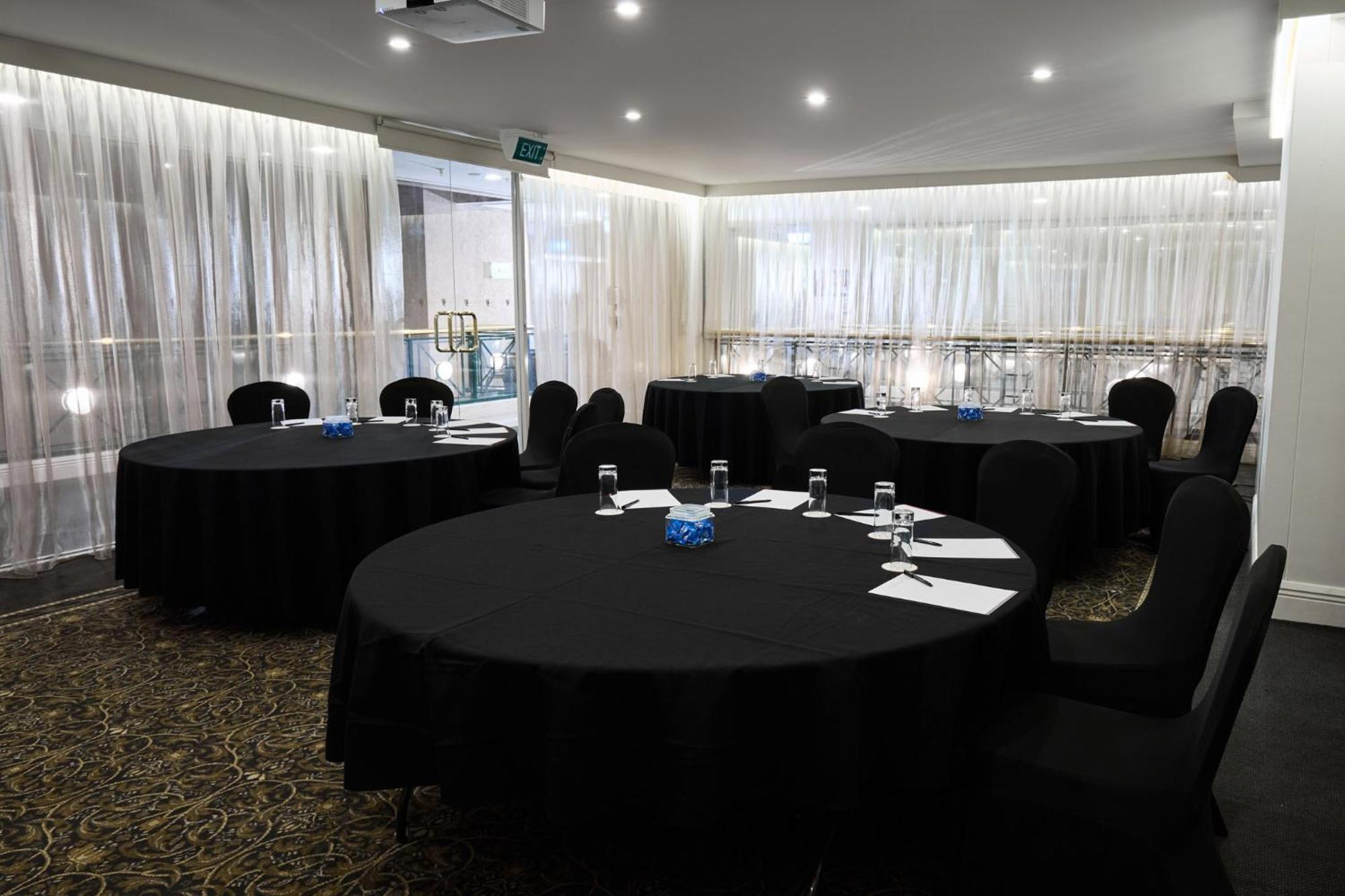 Stamford Plaza Melbourne Hotel Exterior foto The photo shows a meeting or conference room set up with several round tables covered in black tablecloths. Each table is accompanied by black chairs. There are some white notepads and pens placed on the tables, and a small decorative item, possibly 