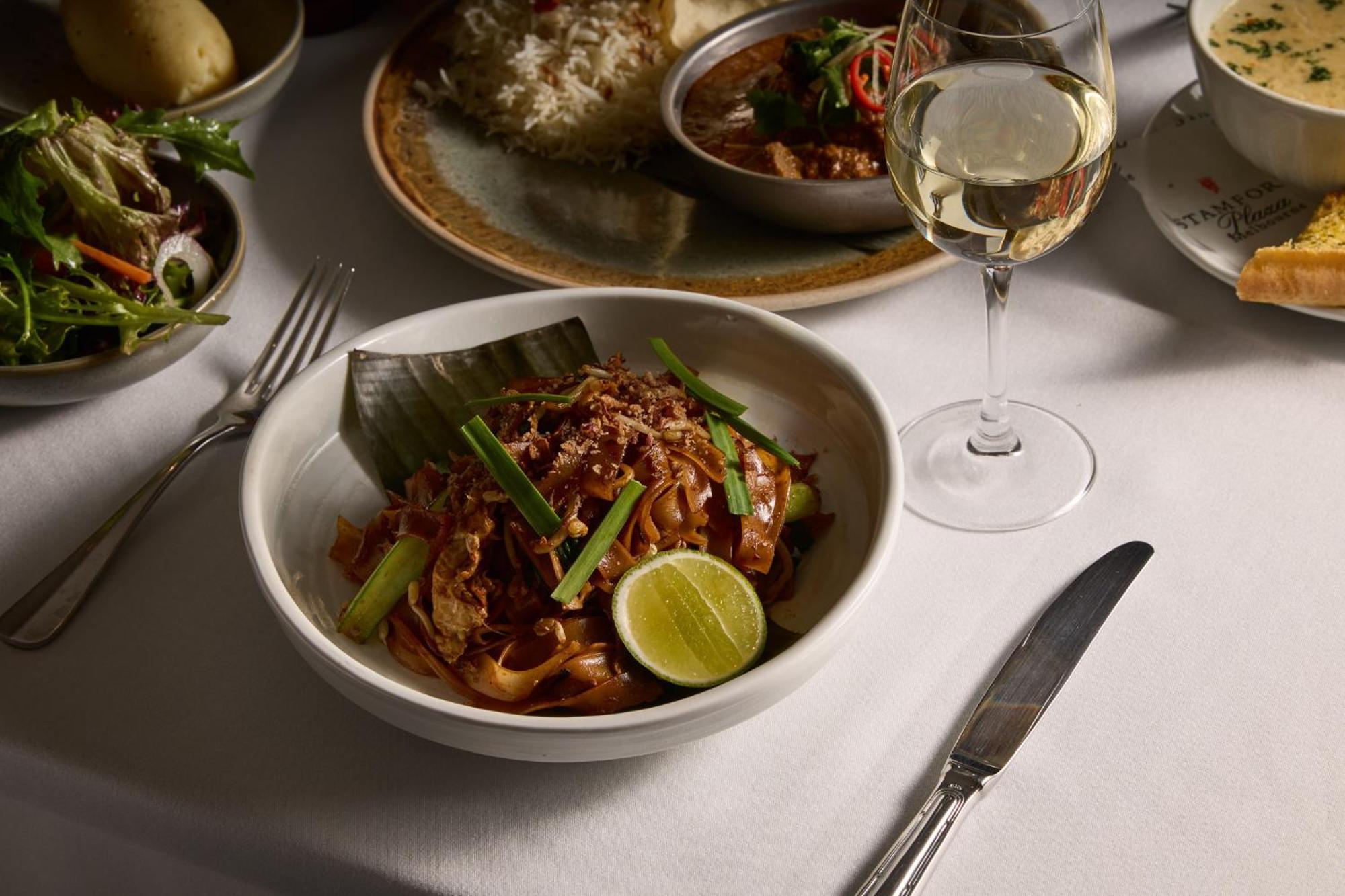 Stamford Plaza Melbourne Hotel Exterior foto The photo features a beautifully arranged dining table with several dishes. In the foreground, there is a bowl of noodles topped with green onions and garnished with a lime wedge. The noodles appear to be stir-fried and have a rich color. Next to the